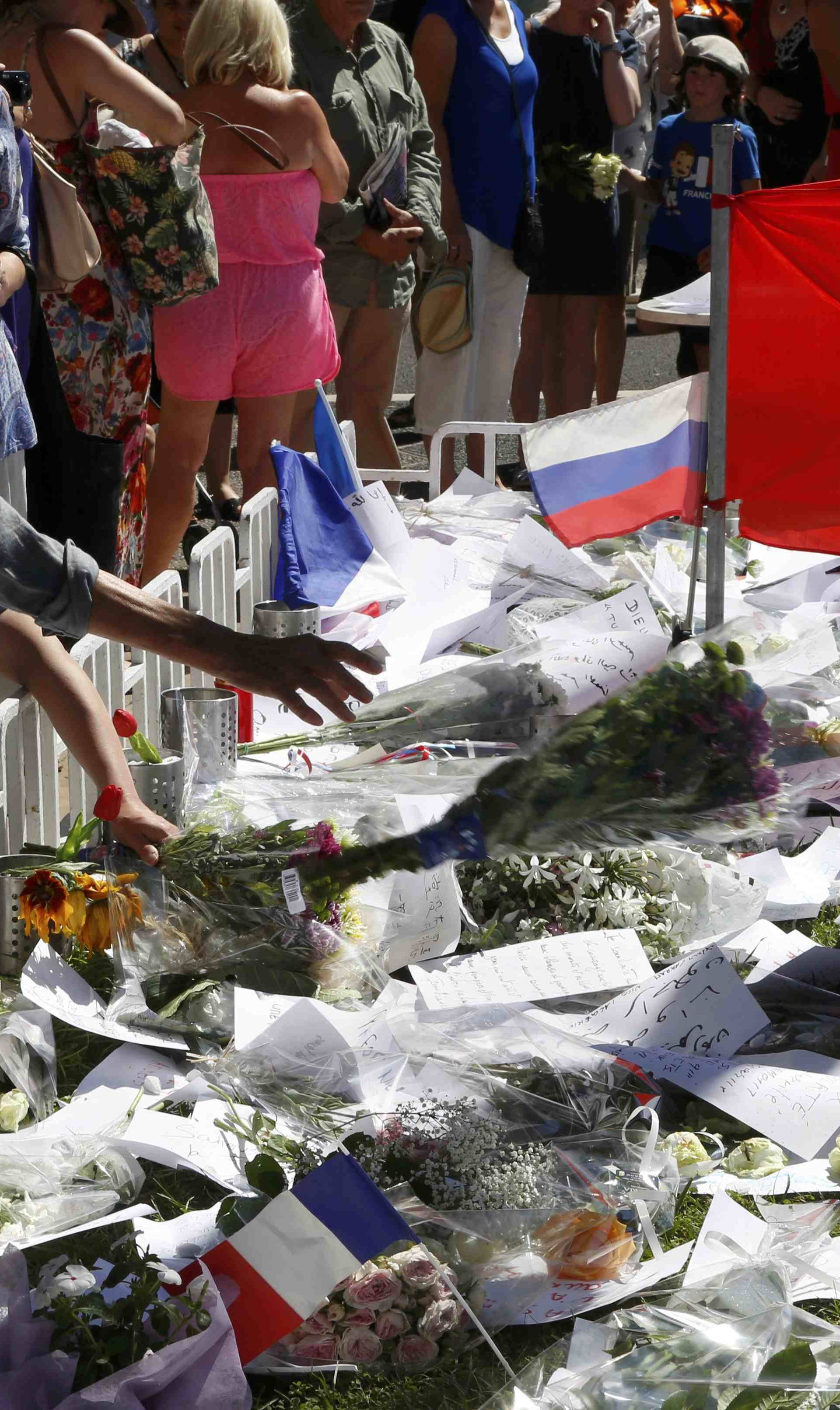A woman adds a bouquet of flower in tribute to victims, two days after an attack by the driver of a heavy truck who ran into a crowd on Bastille Day killing scores and injuring as many, in Nice