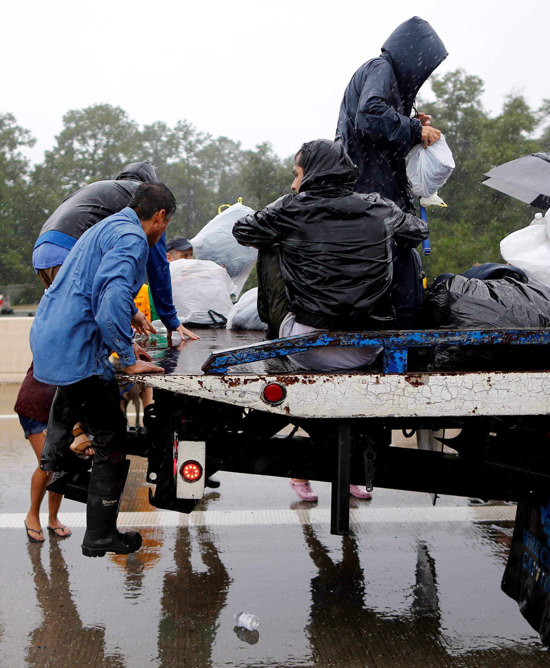 Residents board the bed of a tow truck after being rescued from the flood waters of tropical storm Harvey in east Houston