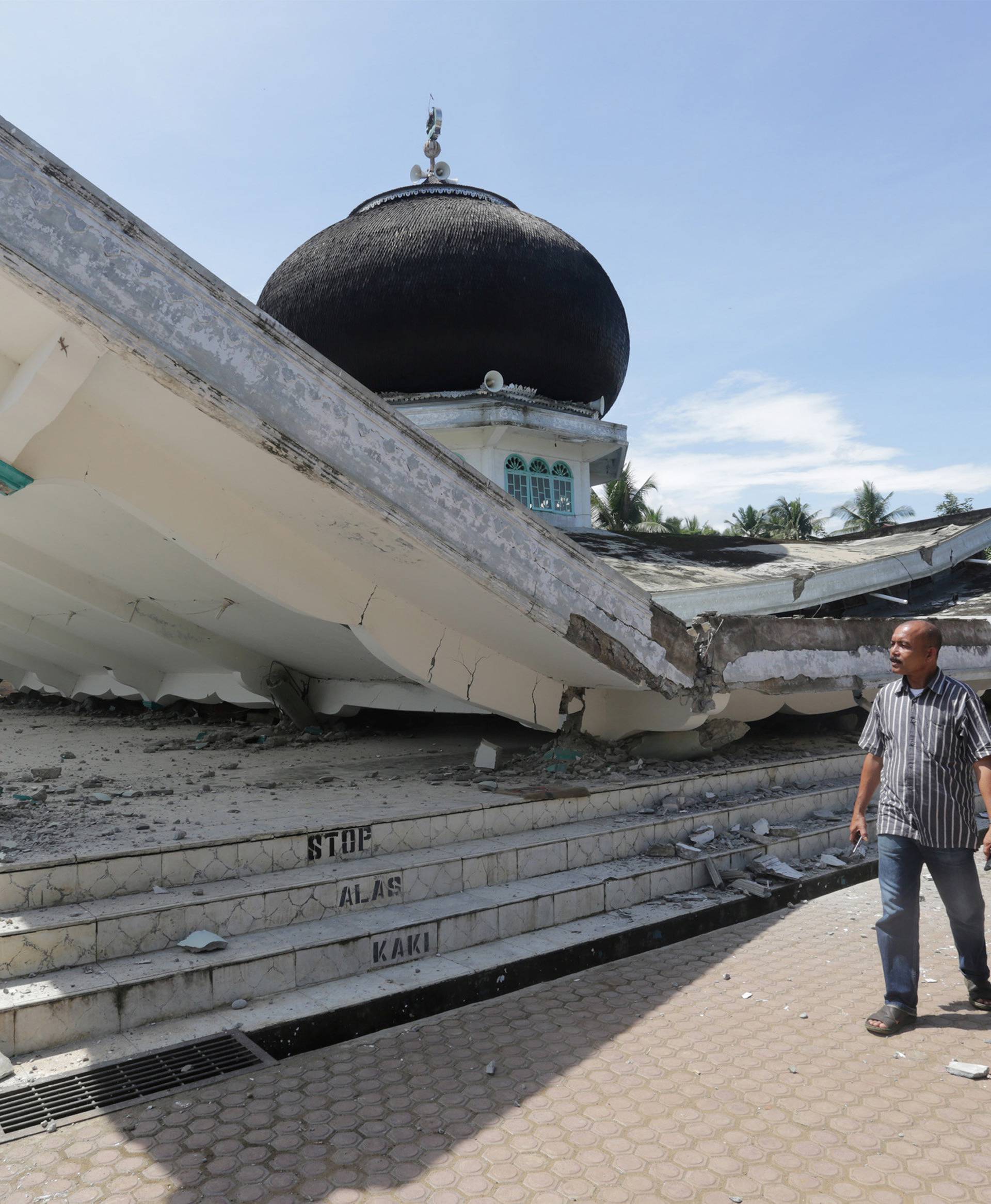 People walk near a collapsed mosque following an earthquake in Meuredu, Pidie Jaya in the northern province of Aceh