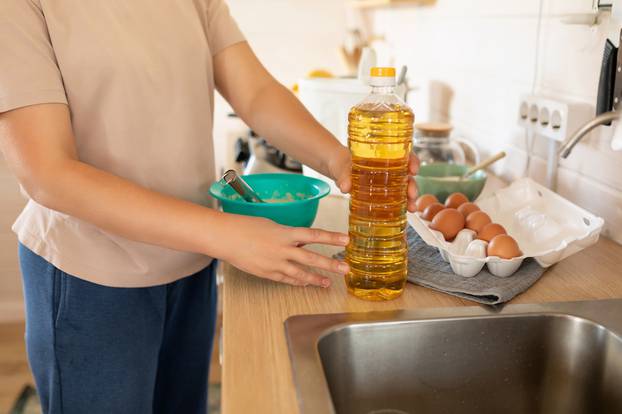 woman adds vegetable oil to pancake batter in the kitchen