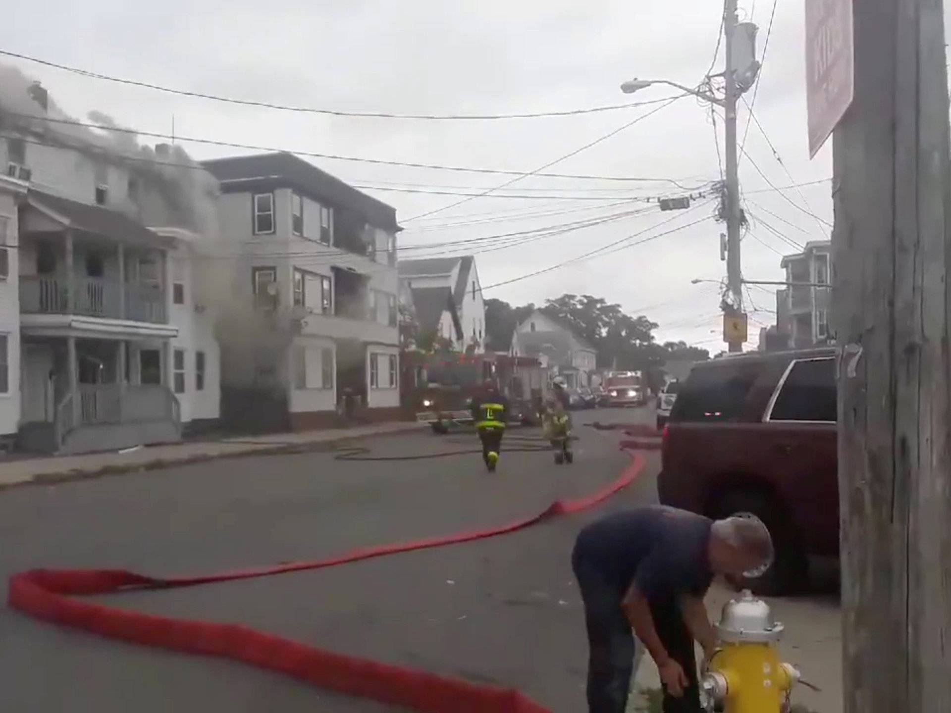 Still image from social media video footage by Boston Sparks shows firefighters working near a building emitting smoke after explosions in Lawrence, Massachusetts