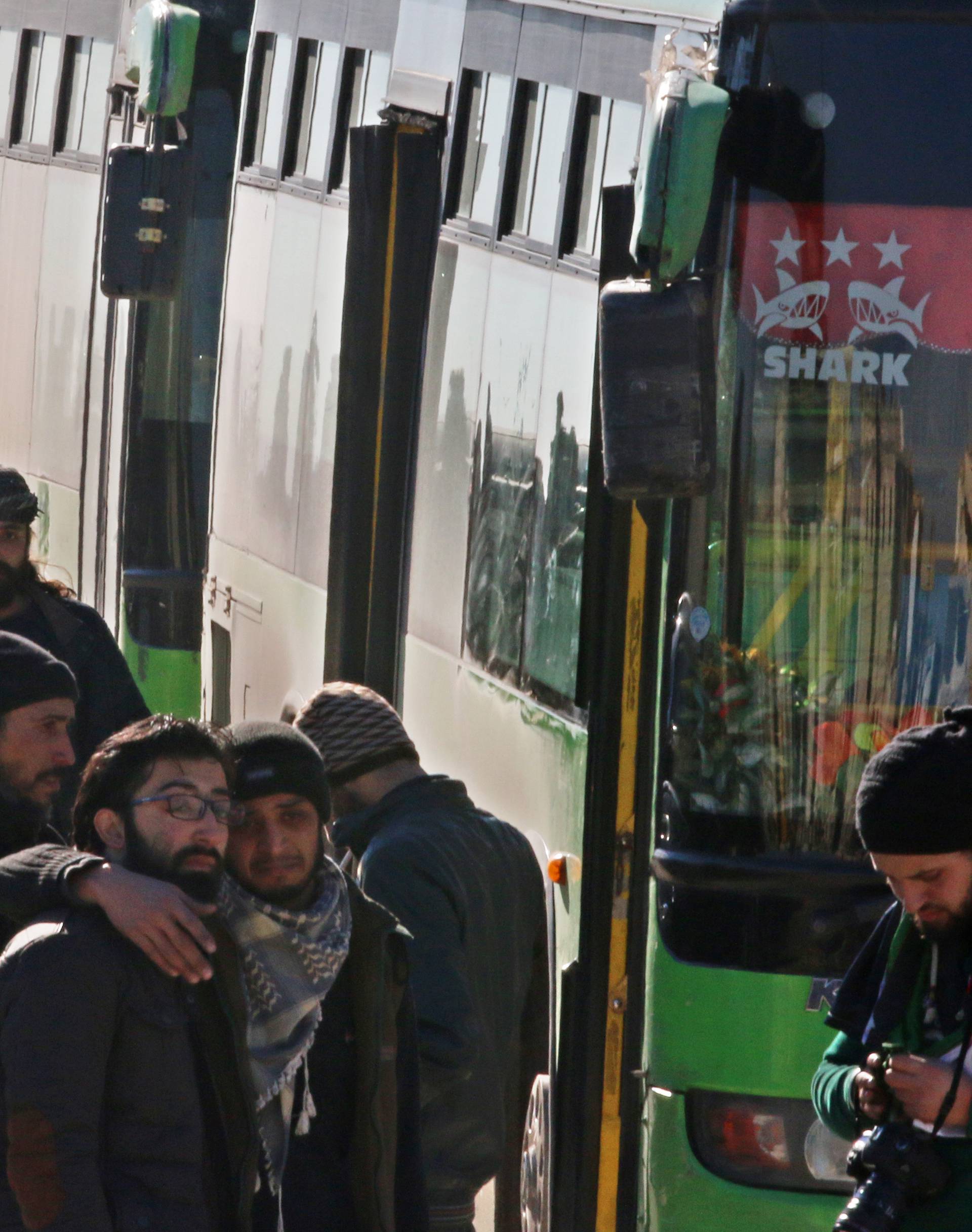 Men react as they stand outside buses evacuating people from a rebel-held sector of eastern Aleppo