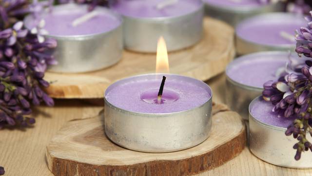 Scented candles on a wooden stand with lilac flowers on the tabl