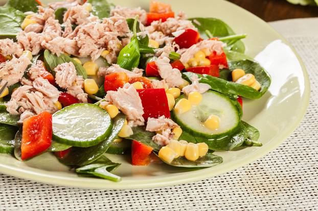Fresh spinach salad with tuna, cucumber, corn, and red paprika on a plate