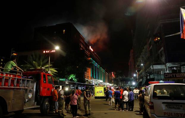 Evacuated employees and guests of hotels stand along a road and watch as smoke billows from a Resorts World building in Pasay City, Metro Manila, Philippines