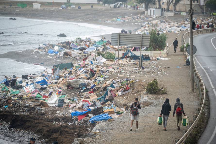 Migrants walk past El Trampolin beach, after police clear the area, in the Spanish enclave of Ceuta