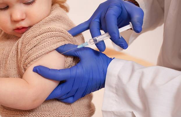 The doctor vaccinates the child against coronavirus. The child is crying and afraid. A man in a robe, hat, mask and gloves makes an injection to the child. Home quarantine