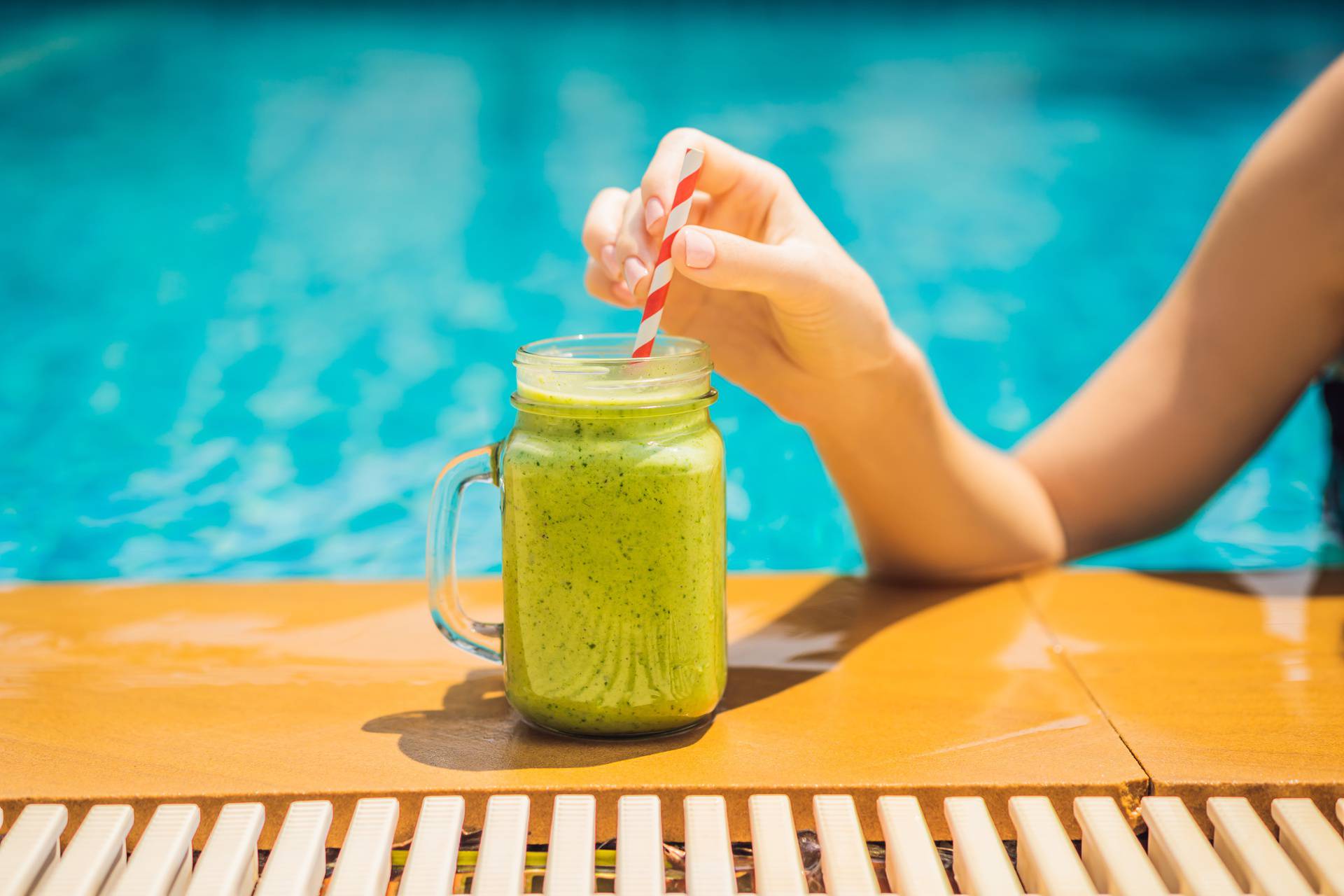 Woman with a green smoothies of spinach and banana on the background of the pool. Healthy food, healthy smoothies