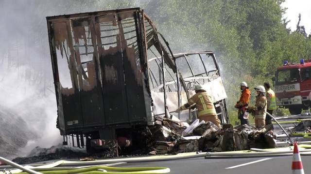 Firefighters walk at the site where a coach burst into flames after colliding with a lorry on a motorway near Muenchberg