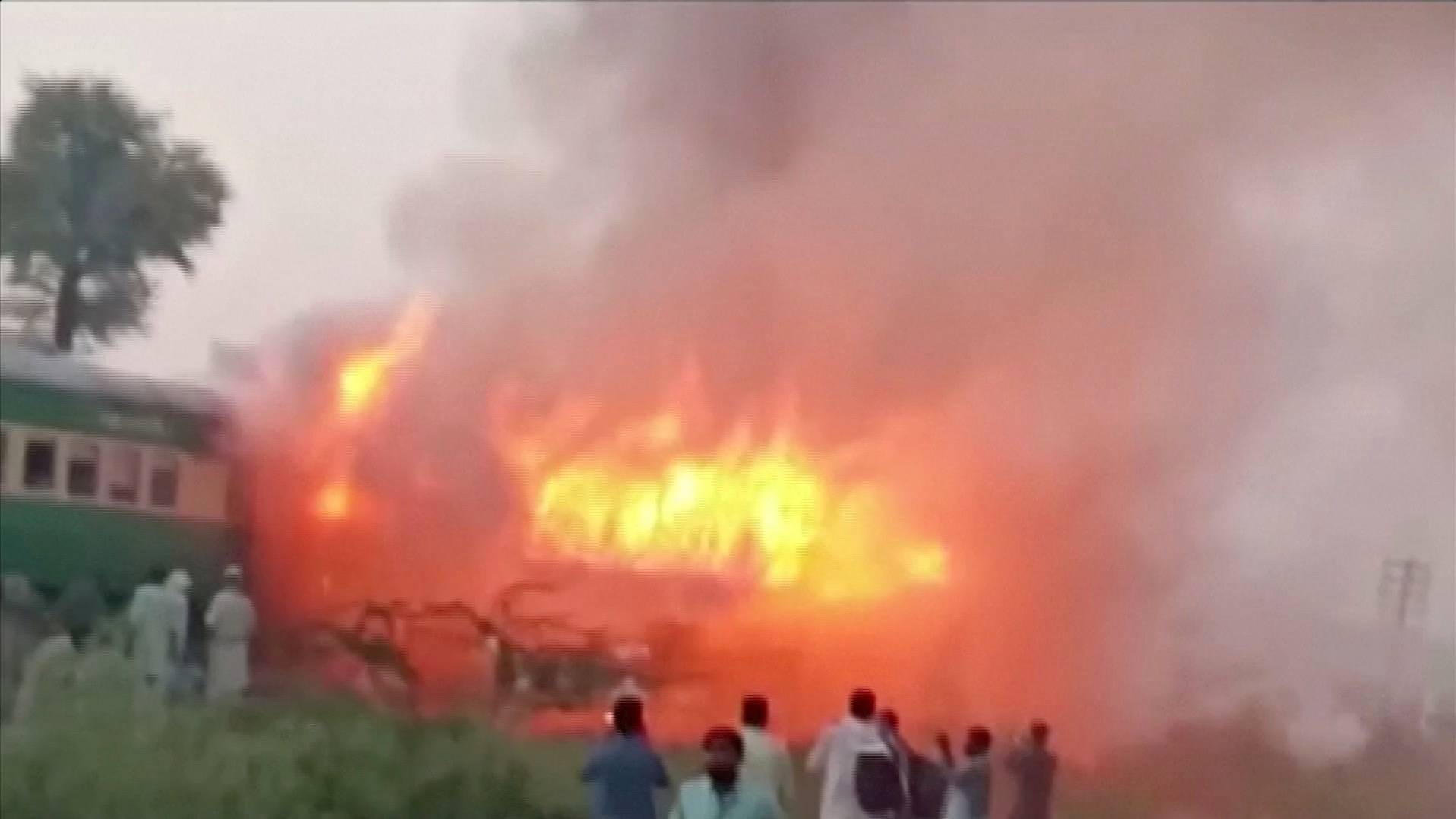 Video grab of people watching fire burn a train after a gas canister passengers were using to cook breakfast exploded, near the town of Rahim Yar Khan