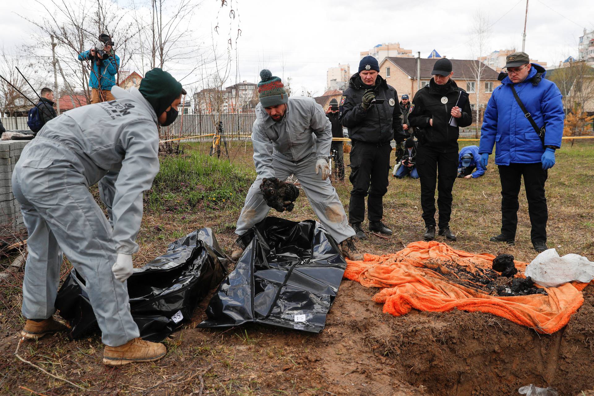 Ukrainian forensics investigators place remains of burned civilians exhumed from a grave in body bags, in the town of Bucha