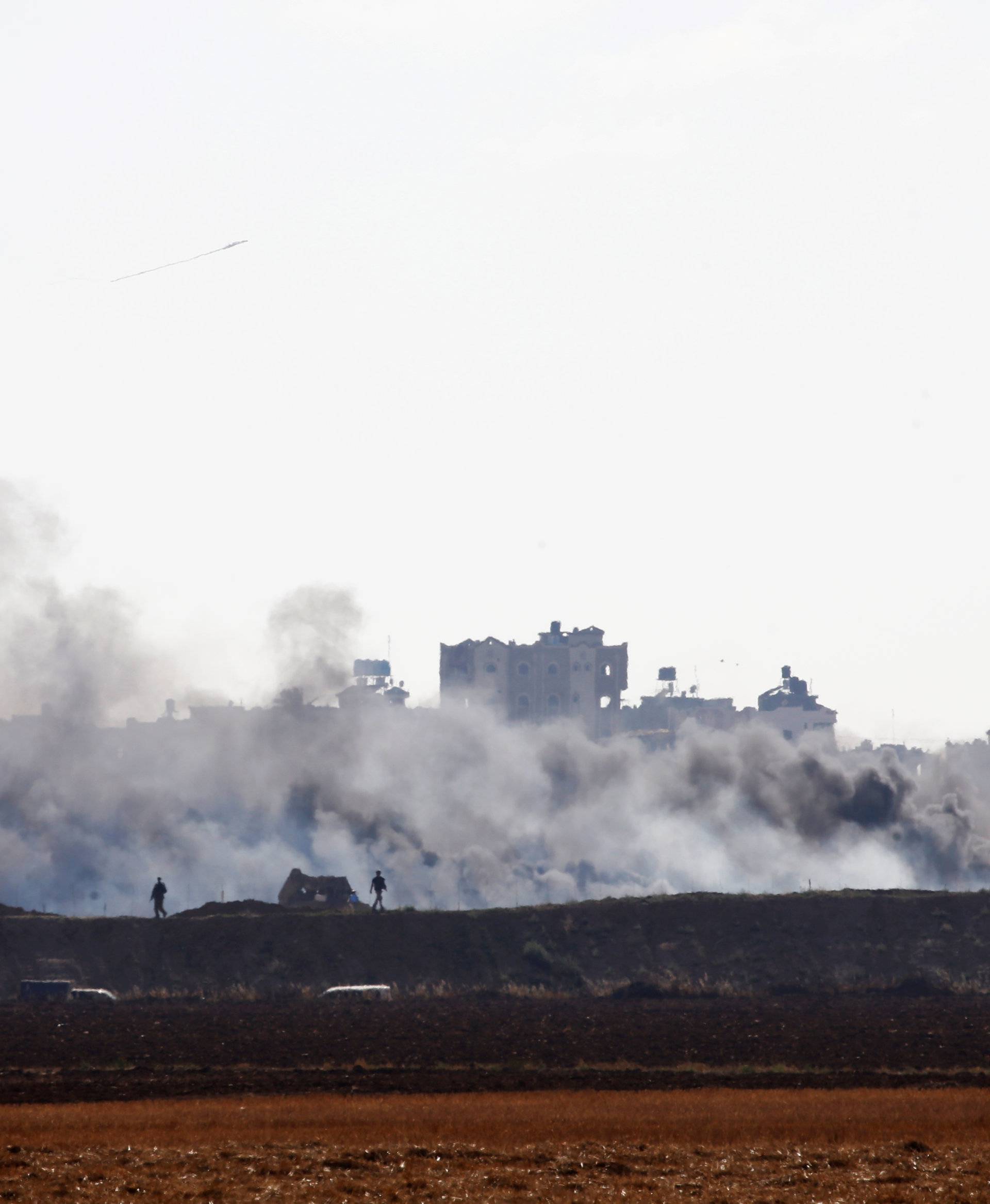 Israeli soldiers walk next to the border between Israel and Gaza as smoke can be seen in the Gaza Strip from the Israeli side