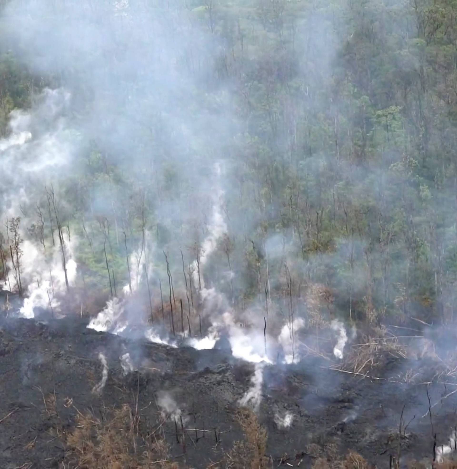 Aerial image of molten rock flowing and bursting to the surface threatening homes in a rural area in Hawaii