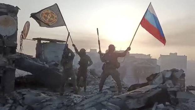 Wagner mercenary group fighters wave flags on top of a building in an unidentified location