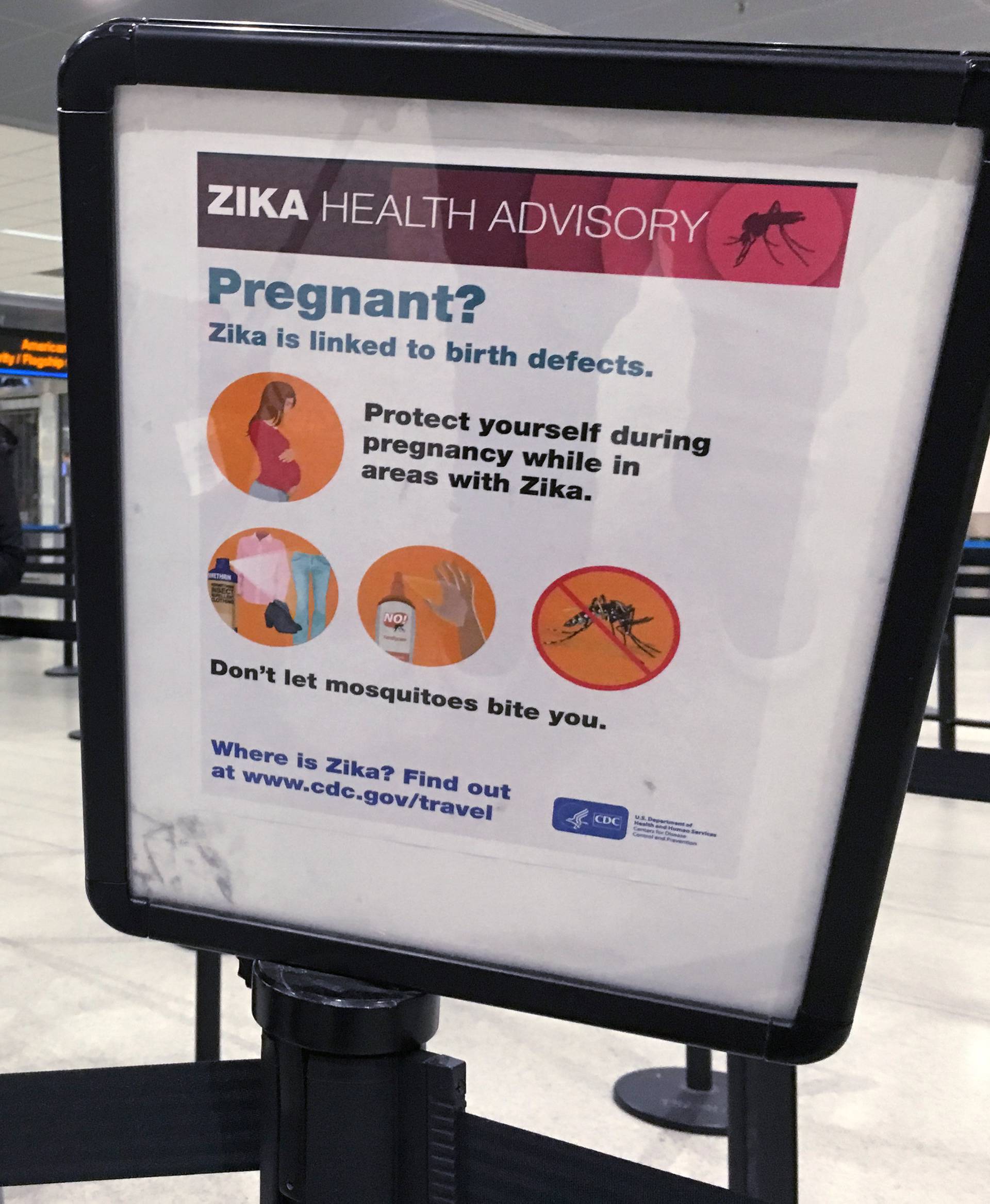 A woman looks at a Center for Disease Control (CDC) health advisory sign about the dangers of the Zika virus as she lines up for a security screening at Miami International Airport in Miami