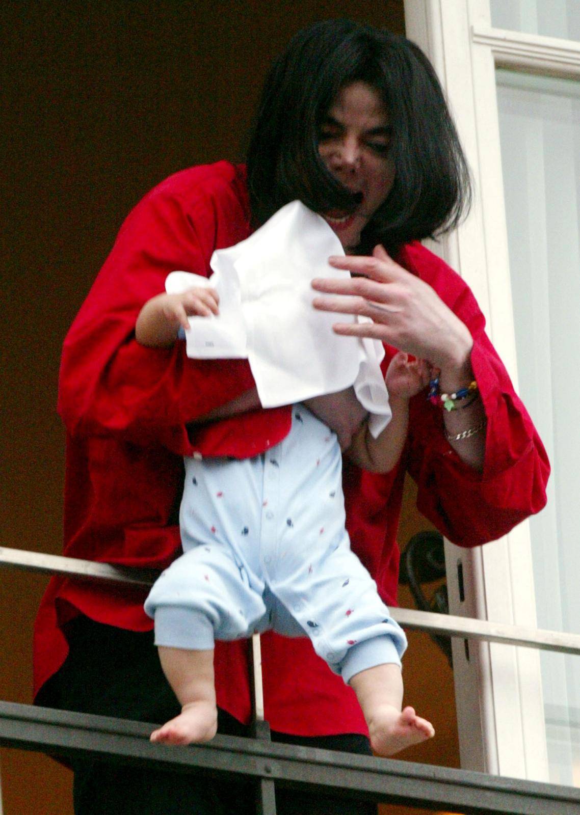 FILE PHOTO: Michael Jackson holds an unidentified child, covered with a towel, as he looks down to fans out of a window after he arrived at a Berlin hotel