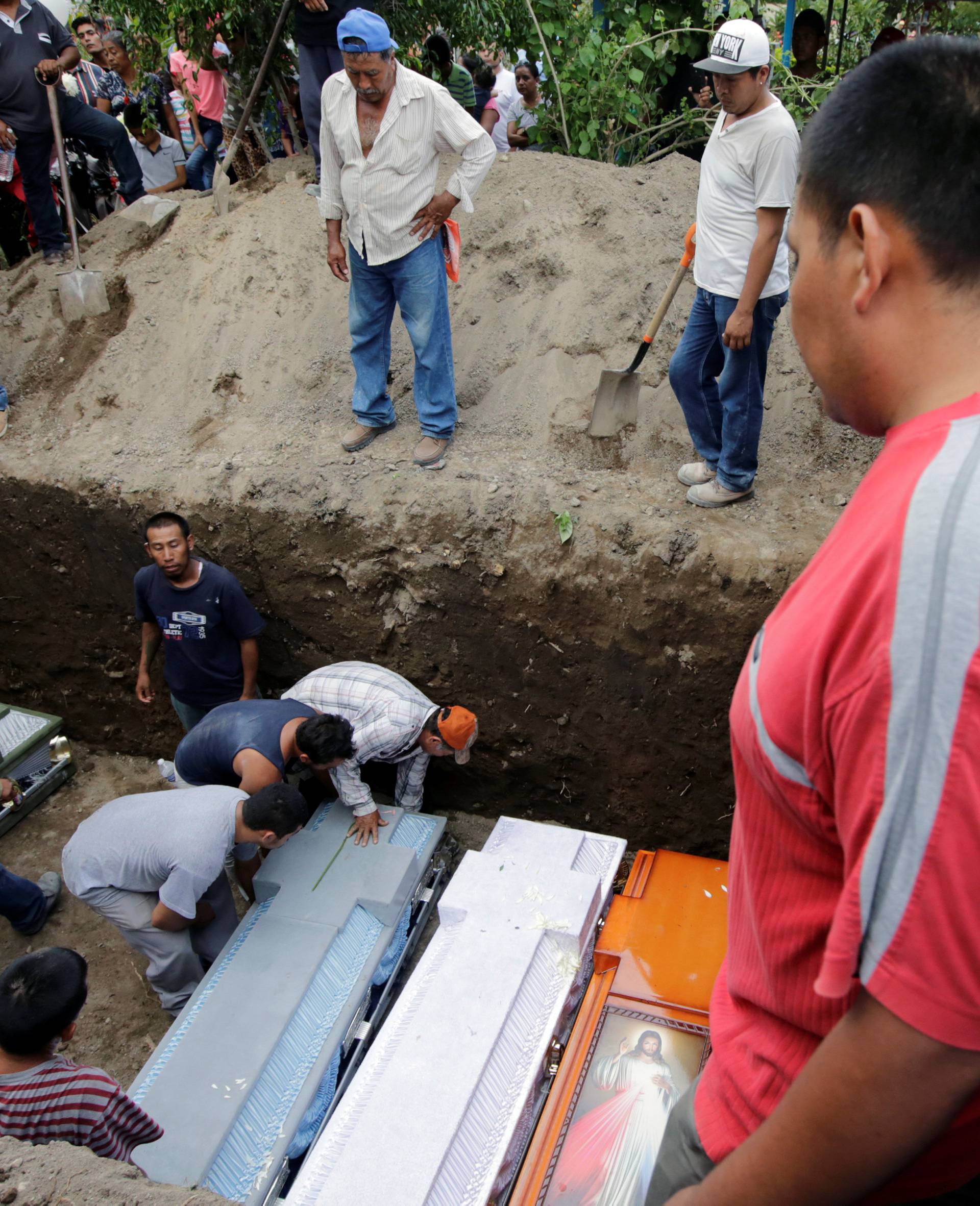 People arrange caskets of earthquake victims in a grave, in Atzala
