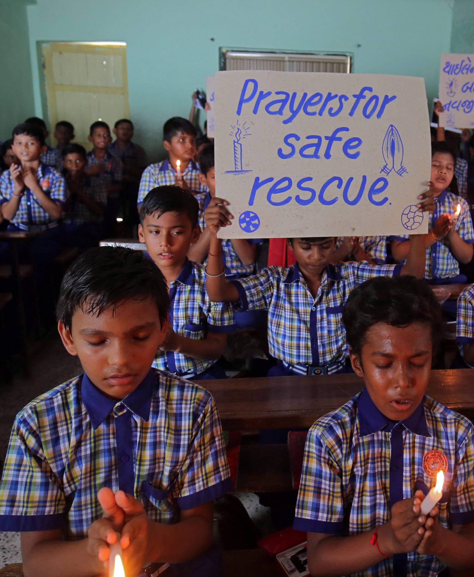 Schoolchildren pray for the schoolboys who are trapped inside a flooded cave in Thailand's northern province of Chiang Rai, at a school in Ahmedabad