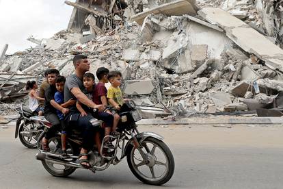 Palestinians ride a motorcycle past the site of an Israeli air strike in Gaza