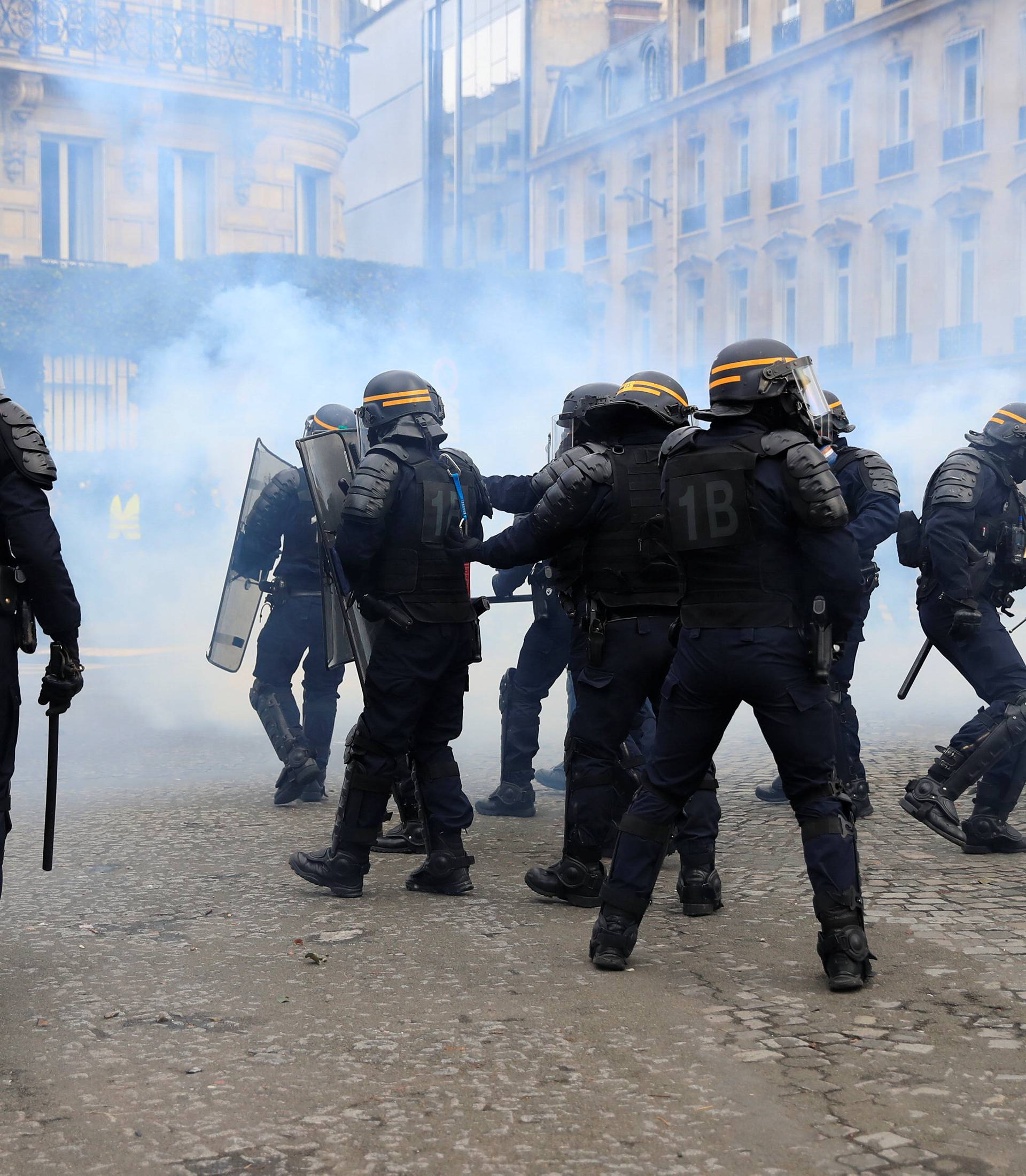 Riot policemen react to tear gas during a demonstration by the "yellow vests" movement in Paris