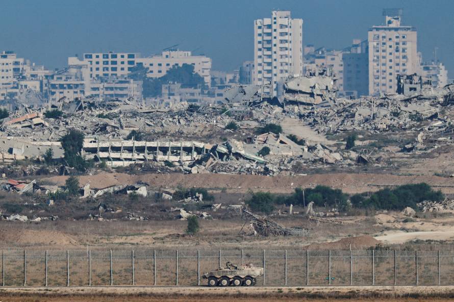 An Armored Personnel Carrier manoeuvres along the Israeli side of the border, as destruction in Gaza is seen in the background