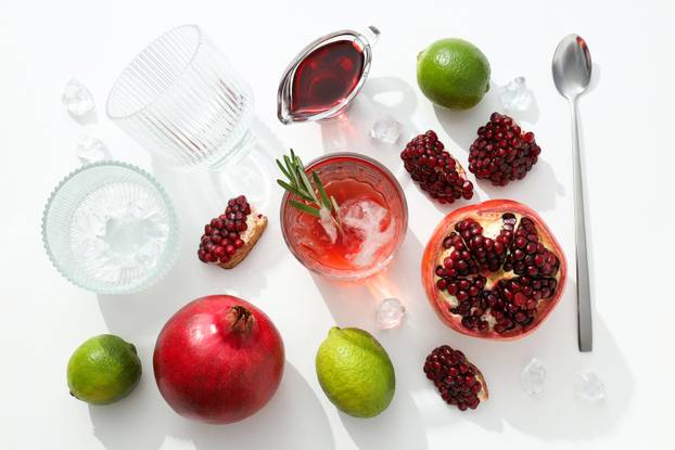 Red cocktail with fresh pomegranate and lime on a white backgrou