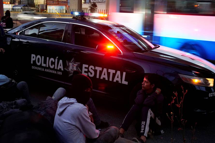 Migrant Nery Josvel from Honduras sits beside a police car as he waits for transportation during his journey towards the United States, in Mexico City