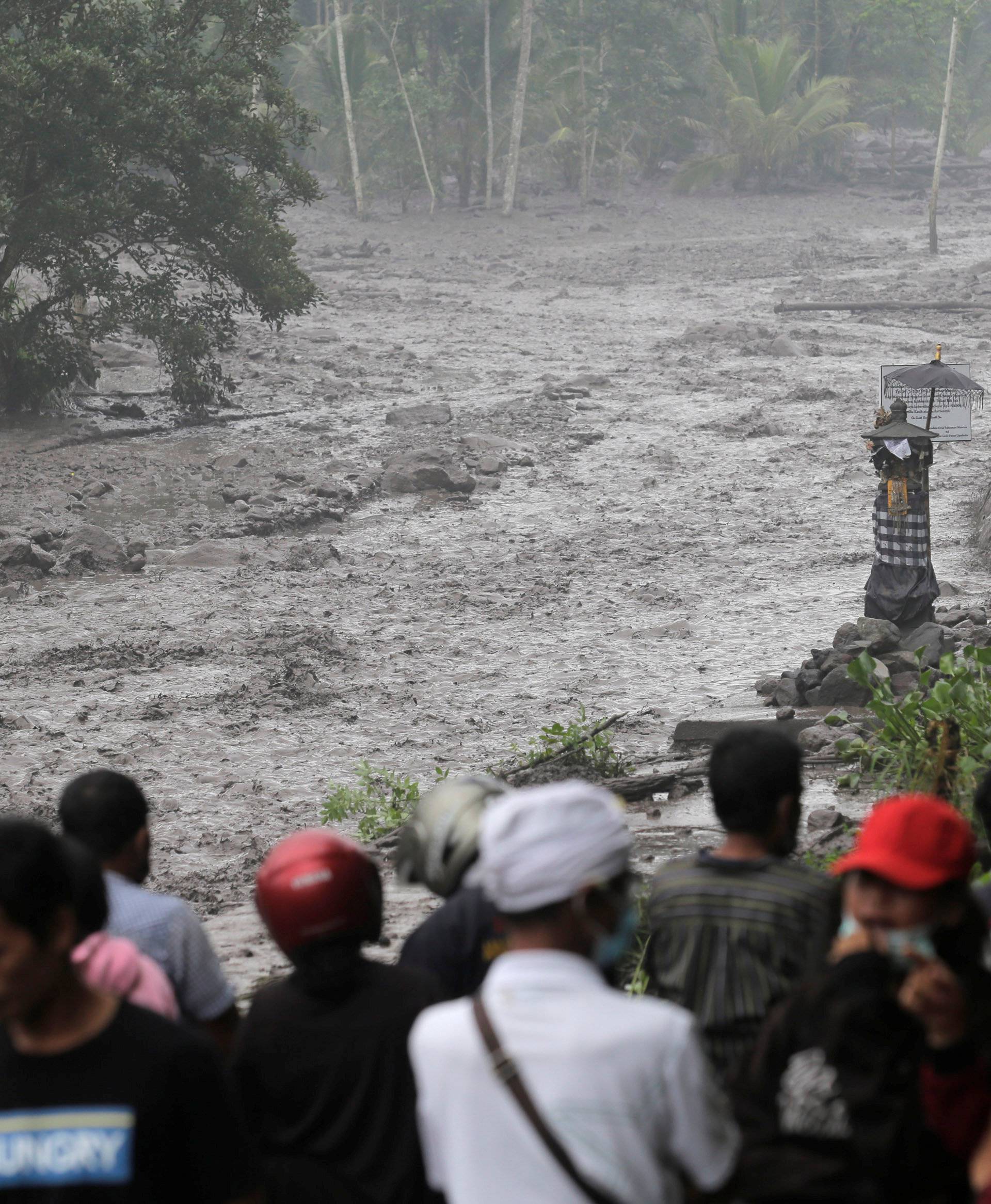 Villagers watch a river overflowing with water mixed with volcanic ash during the eruption of Mount Agung in Karangasem