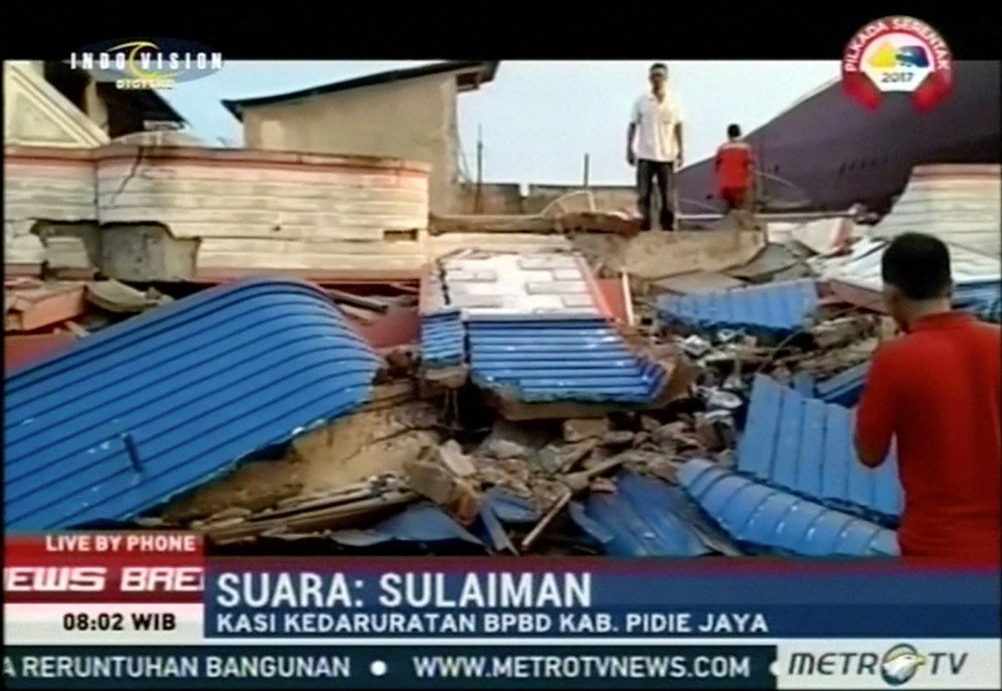 People stand next to rubble of collapsed buildings following an earthquake in Pidie Jaya, Aceh, Indonesia in this still frame taken from video