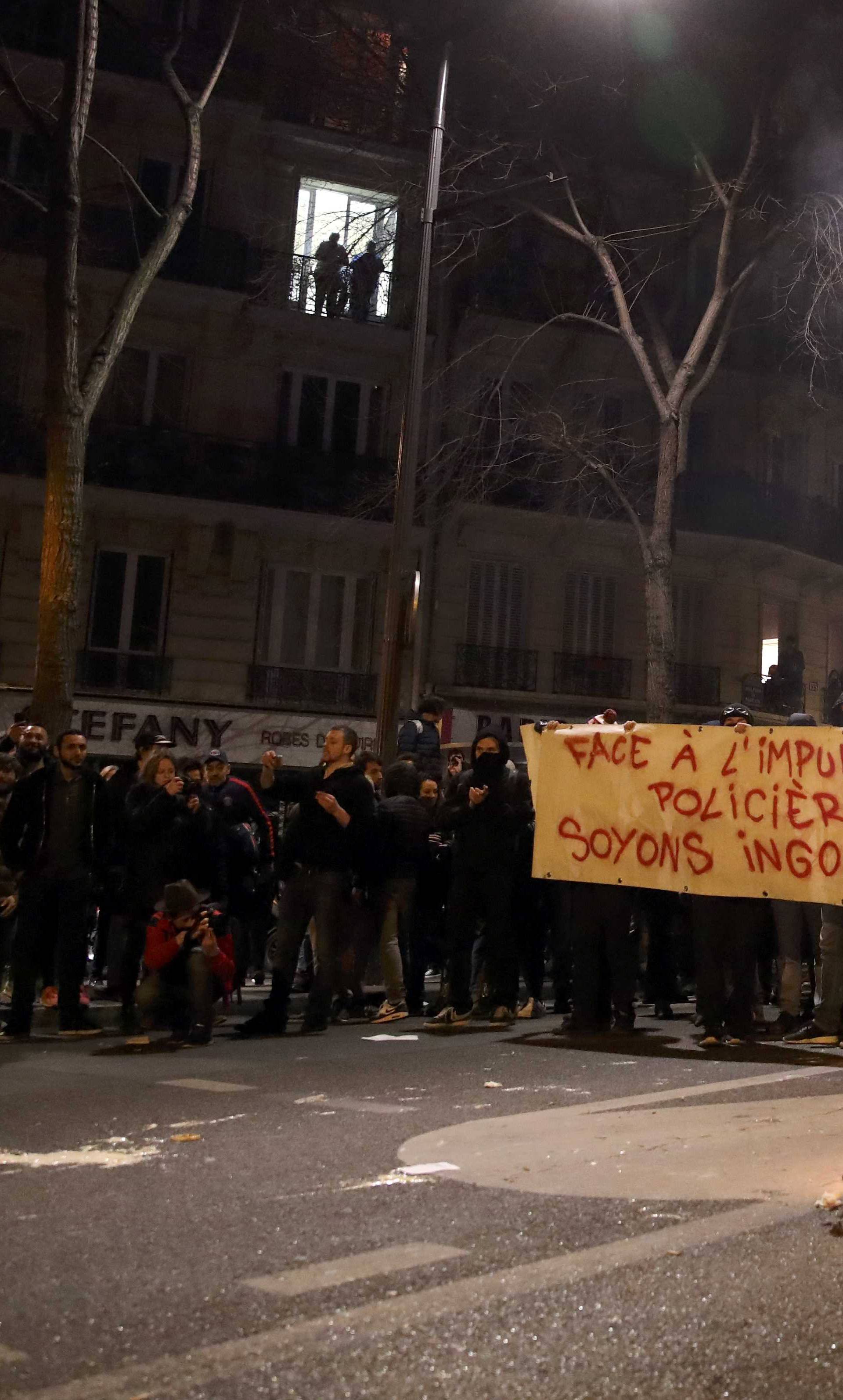 Trash burns on the street as people hold a banners with messages to protest police brutality as they gather at a deomostration in Paris 
