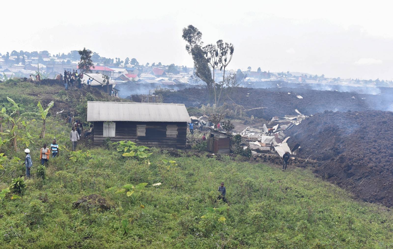 Residents walk near destroyed homes with the smouldering lava deposited by the eruption of Mount Nyiragongo volcano near Goma