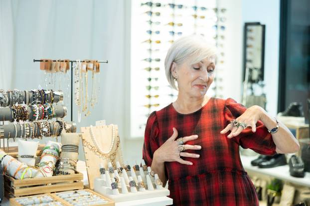 Cheerful elderly woman choosing rings from display with costume jewelry in boutique