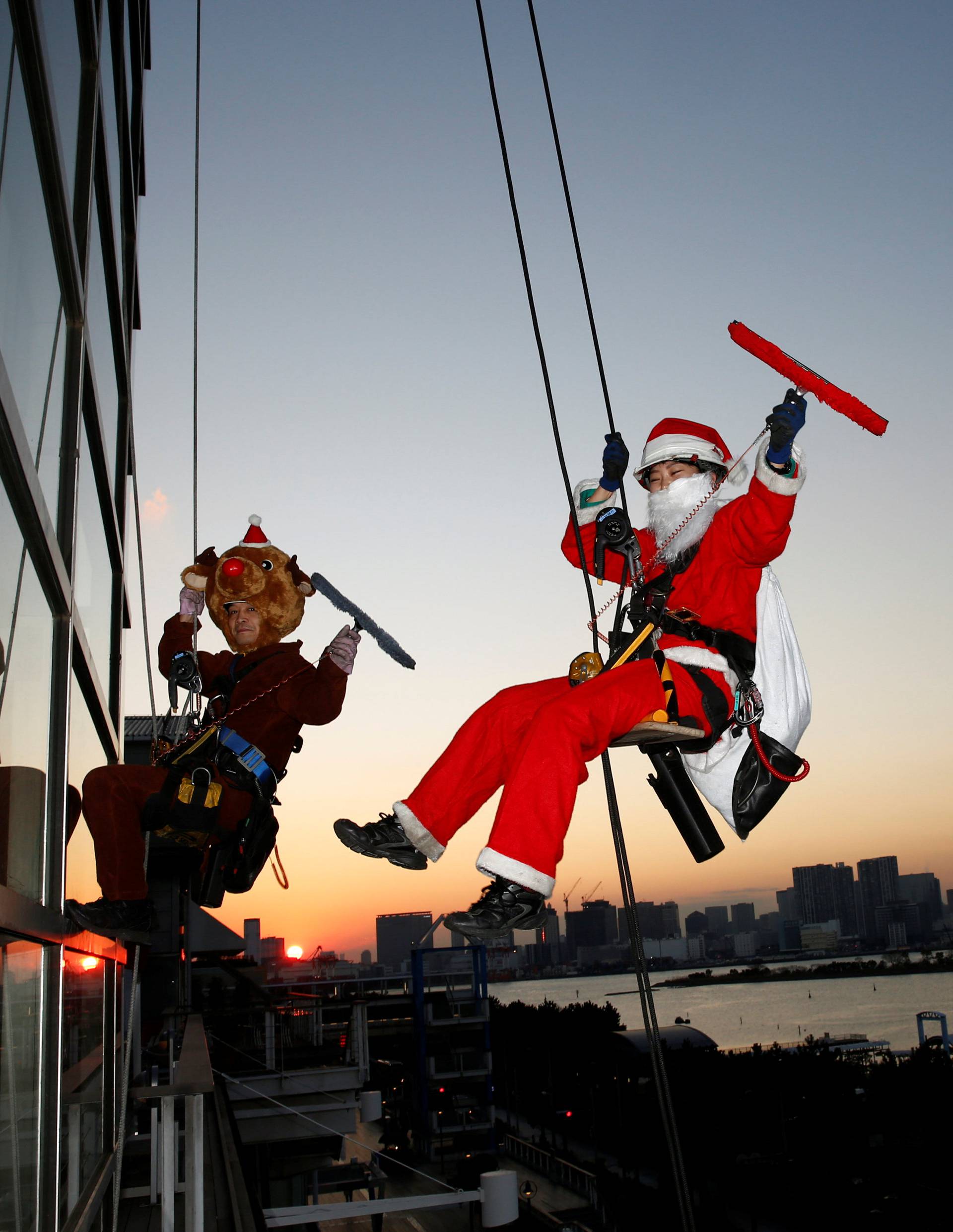 Window cleaners dressed as Santa Claus and a reindeer pose for photographers as they clean a glass window at an event to celebrate the upcoming Christmas at DECKS Tokyo Beach in Tokyo