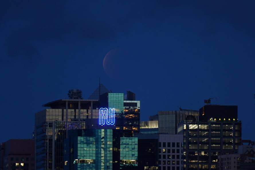 The full moon eclipse, known as the "Super Blood Moon", rises through low clouds above the Eastern District of Hong Kong