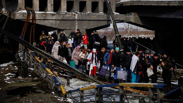 People file across a makeshift river crossing below a destroyed bridge as they flee from advancing Russian troops whose attack on Ukraine continues in the town of Irpin outside Kyiv