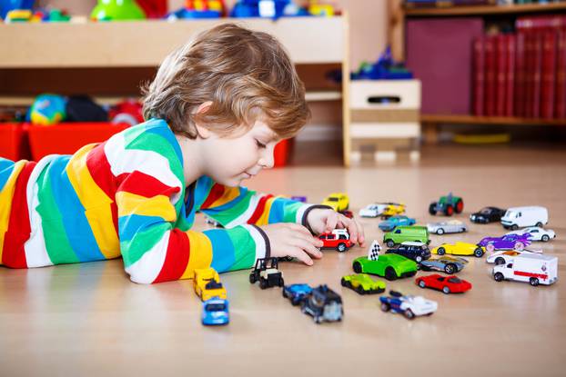 Little blond child playing with lots of toy cars indoor