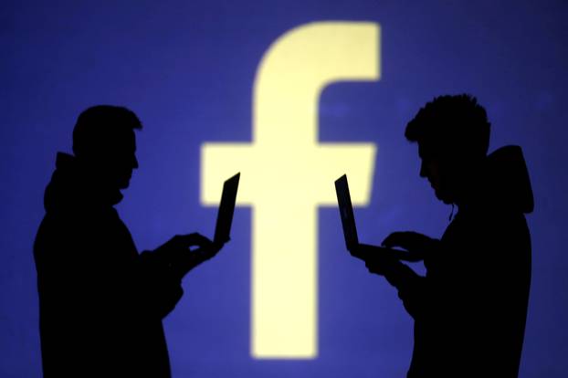 FILE PHOTO: Silhouettes of laptop users are seen next to a screen projection of Facebook logo in this picture illustration