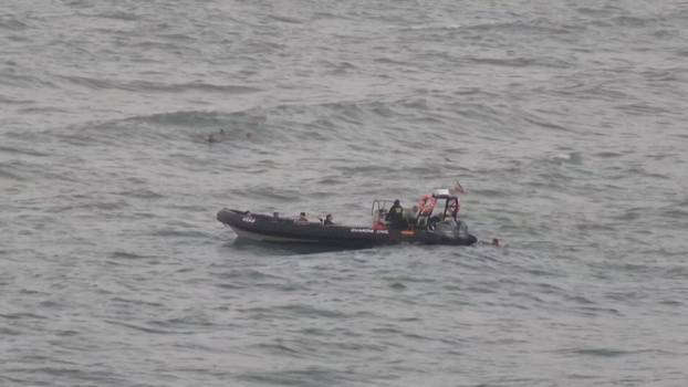 A view shows migrants reaching a police boat, while other group of migrants swim in the background, in Ceuta