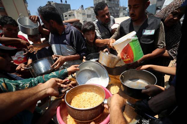 Palestinians wait to receive food cooked by a charity kitchen, in Gaza City