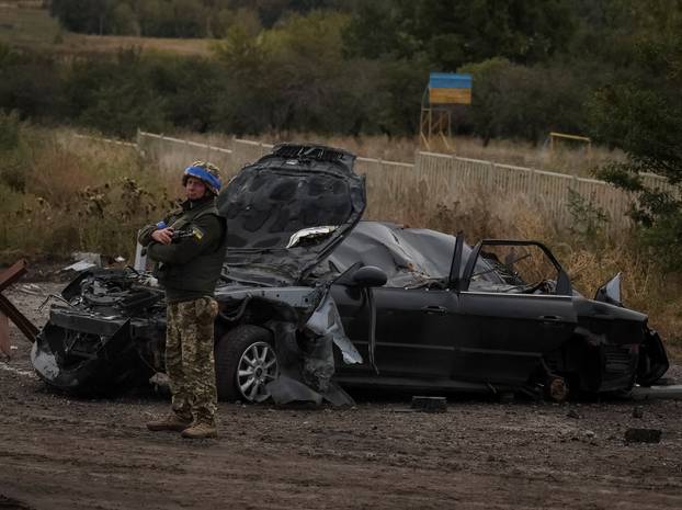 Ukrainian serviceman stands guard near a destroyed car in Kharkiv region