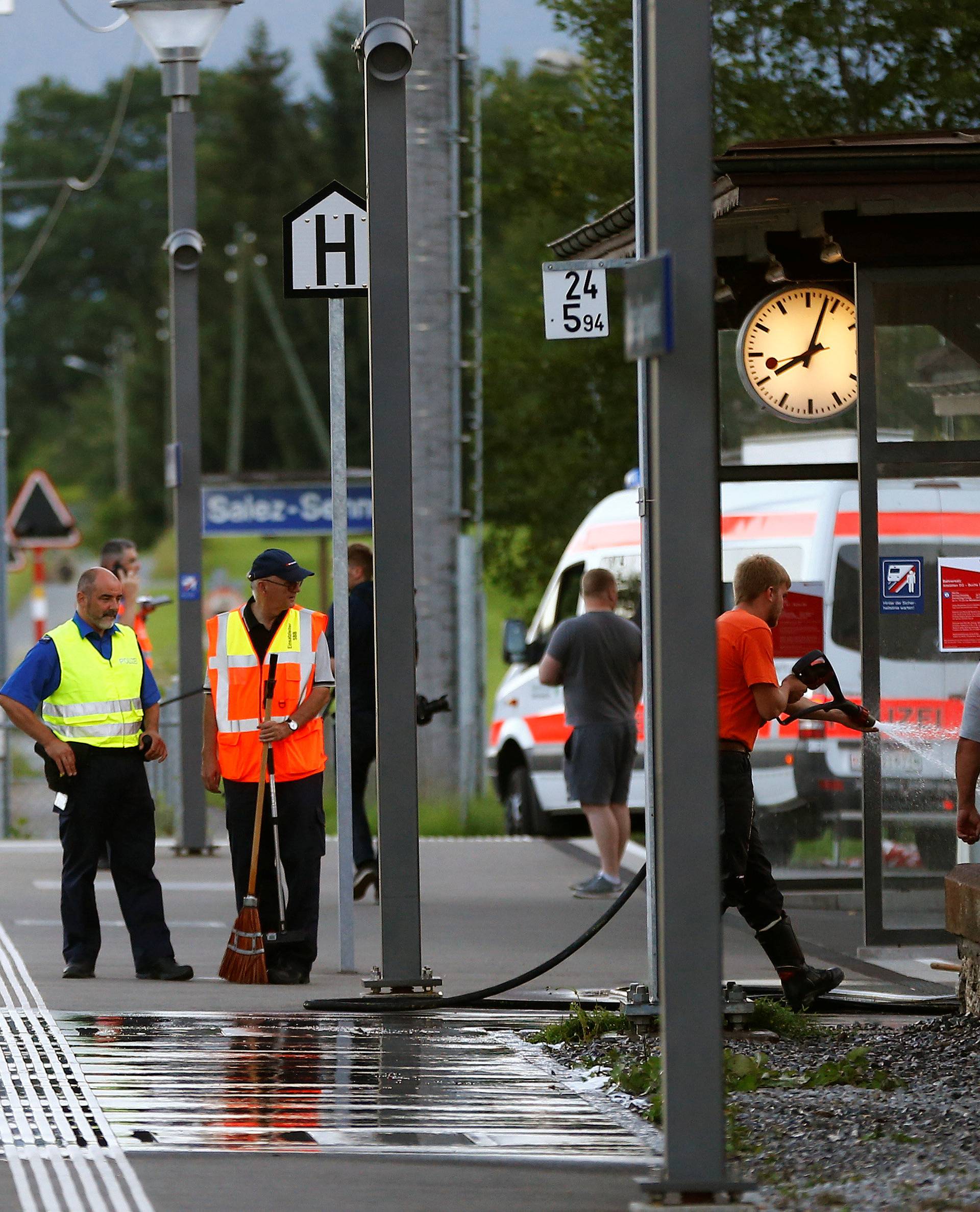 A Swiss police officer stands near workers cleaning a platform after a 27-year-old Swiss man's attack on a Swiss train at the railway station in the town of Salez