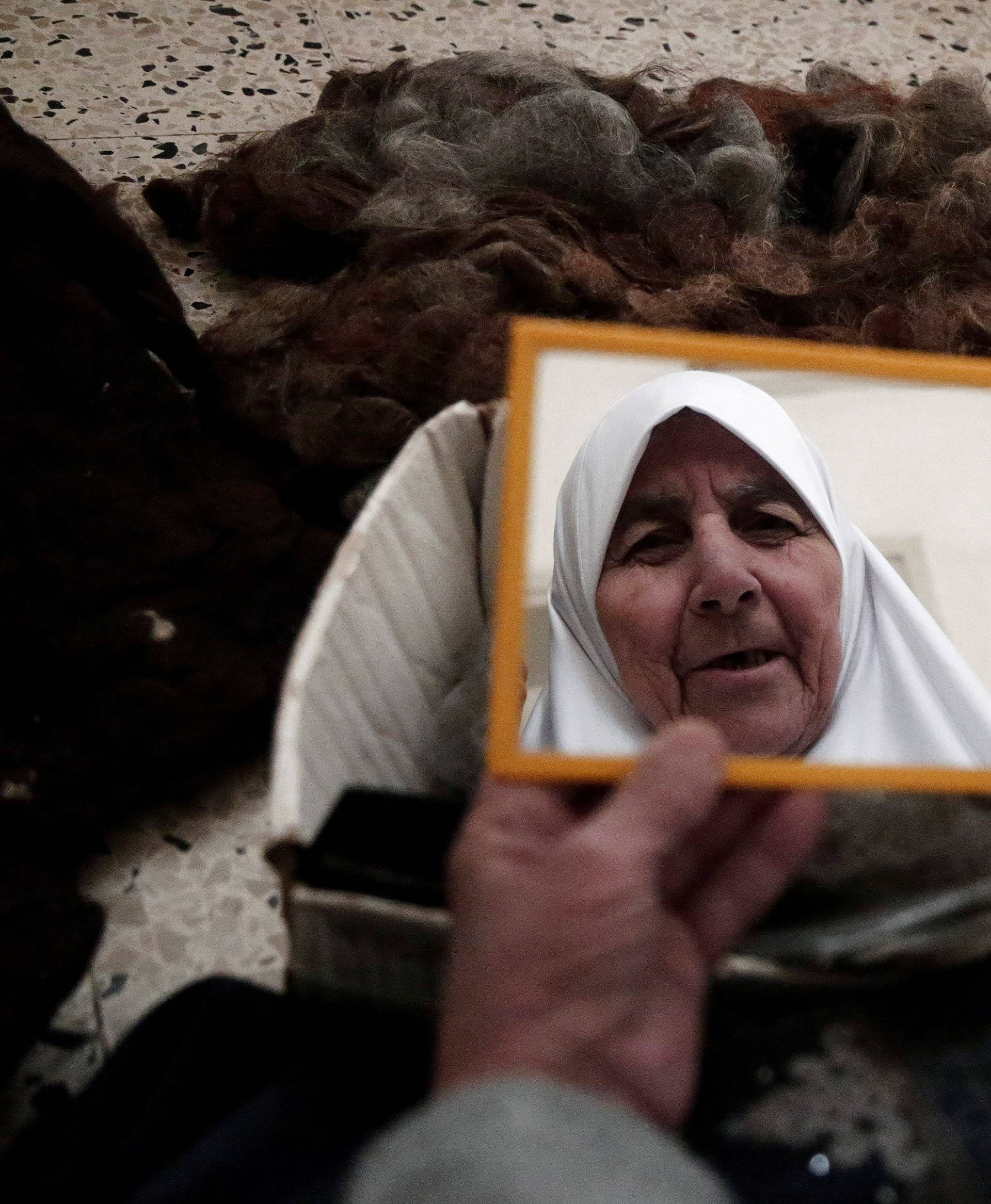 Ezzeya Daraghmeh, an 82-year-old Palestinian woman who said she has kept parts of her hair she cut over 67 years, looks at herself in a mirror as she stuffs a pillow with her hair, in the West Bank town of Tubas