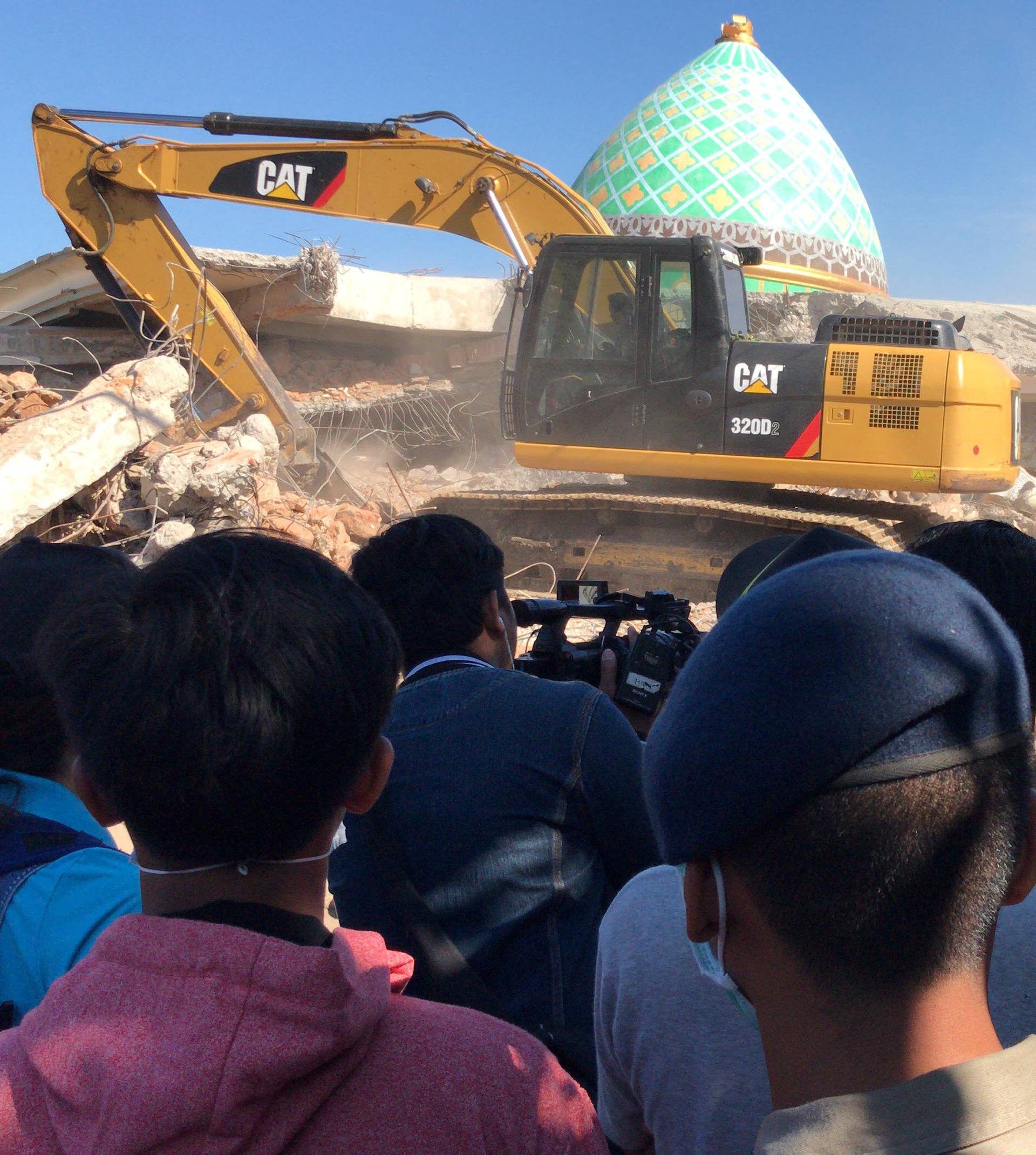 People watch as rescue crews use heavy machinery to search for earthquake victims at Jamiul Jamaah mosque in Pemenang