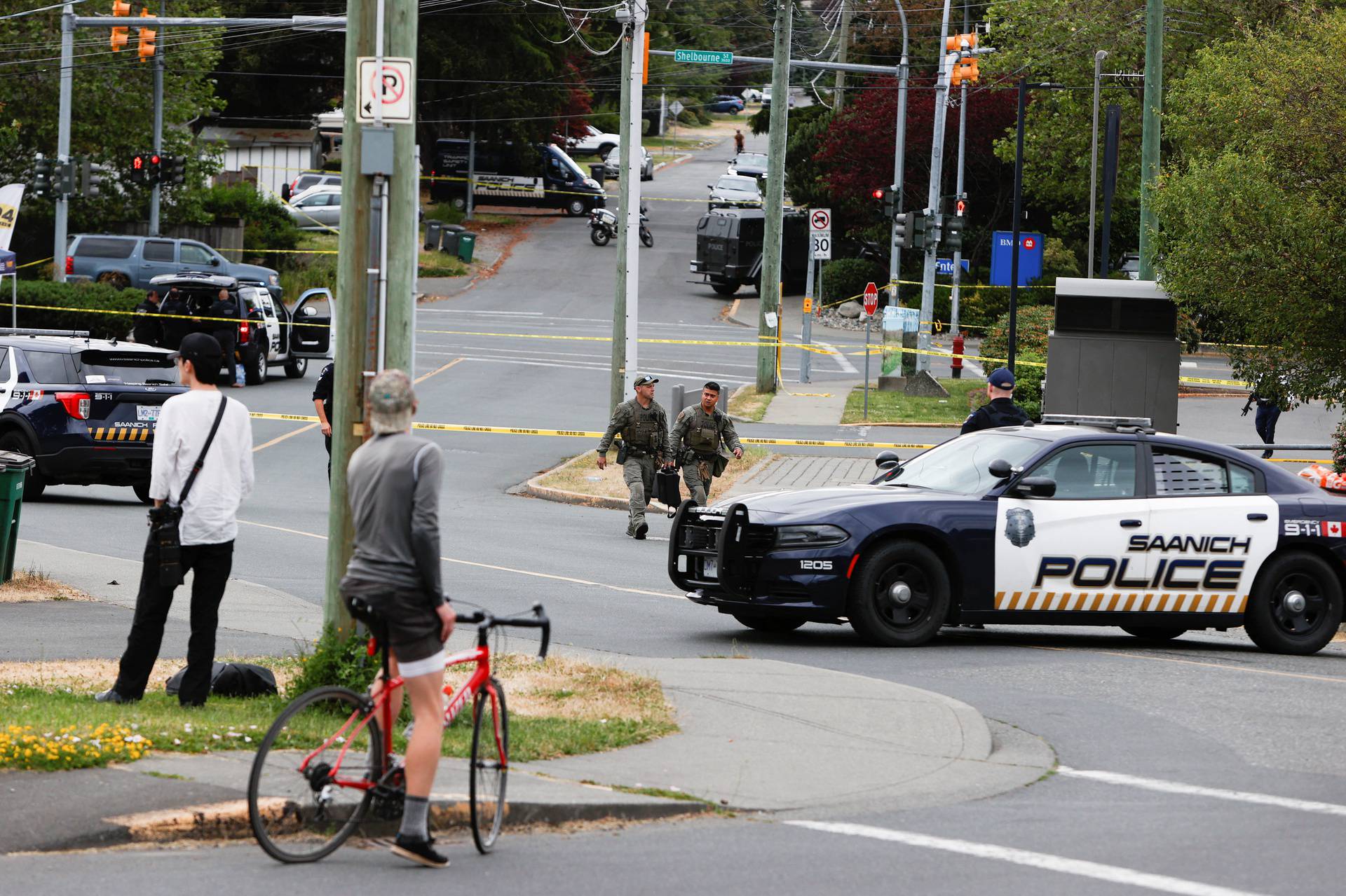 Police officers gather after two armed men entering a bank were killed in a shootout with the police in Saanich