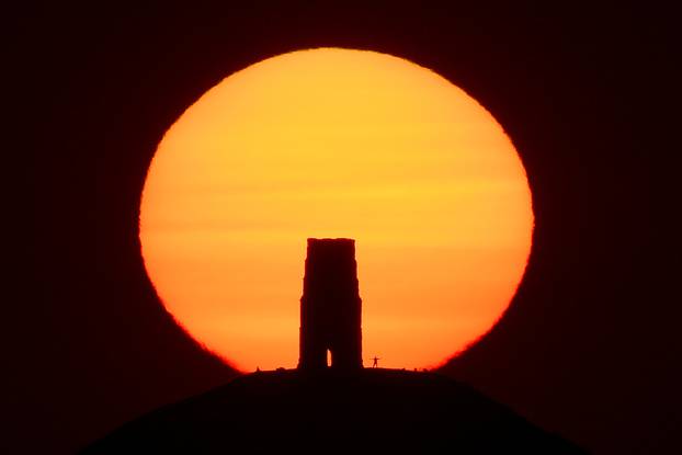A person views the sun rise from beside the remains of Saint Michael's Church on top of Glastonbury Tor, in Glastonbury