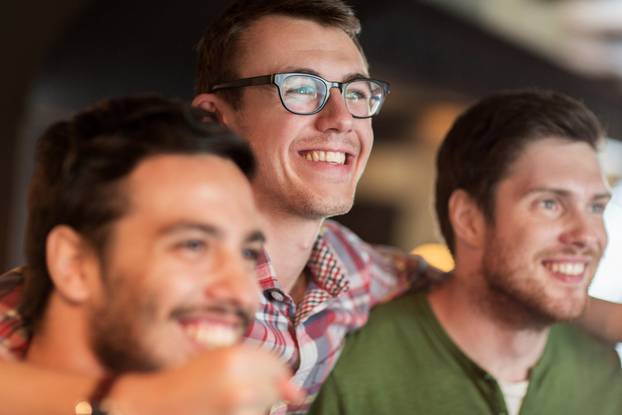 happy male friends watching football at bar or pub