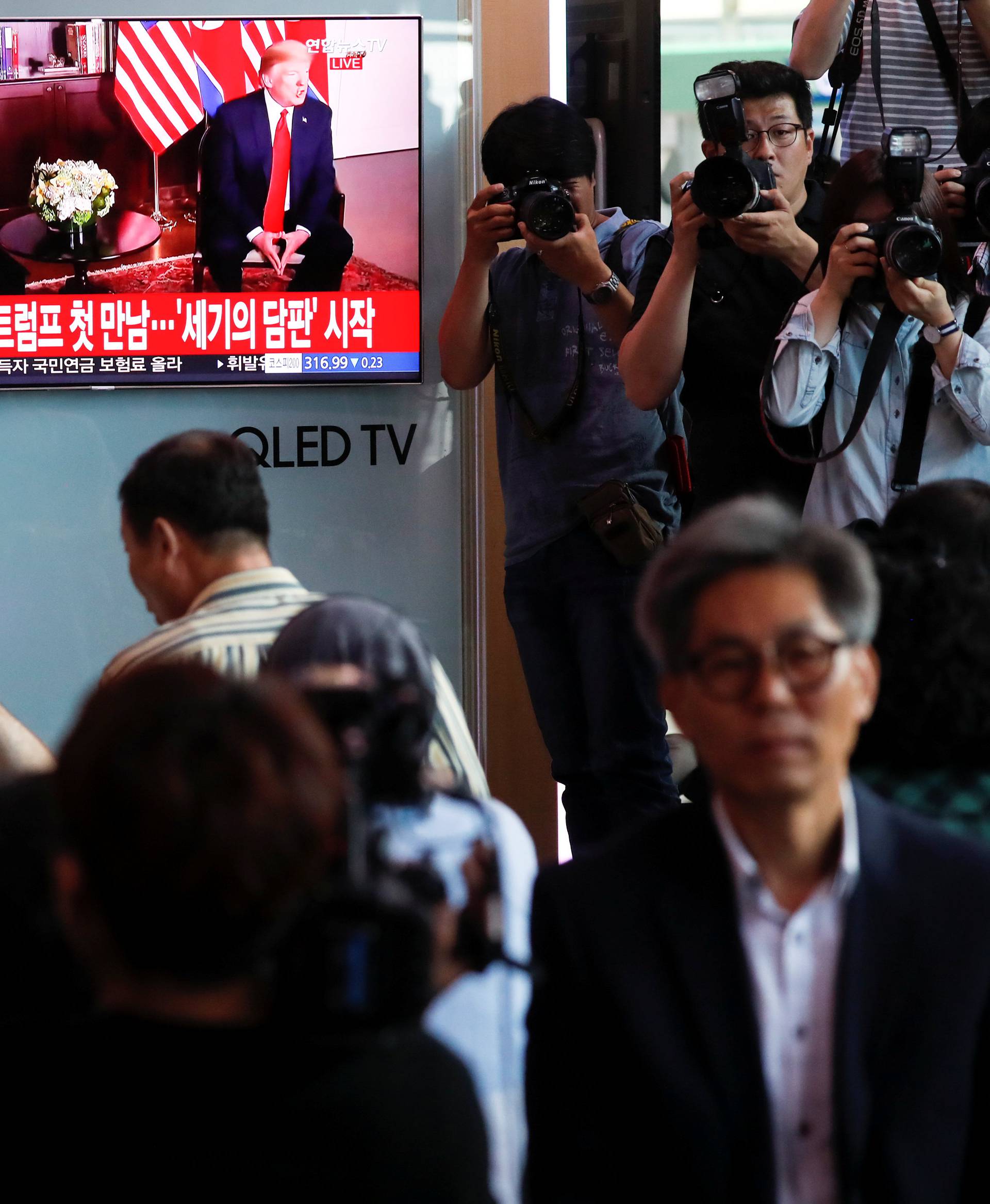 People watch a TV broadcasting a news report on summit between the U.S. and North Korea, in Seoul