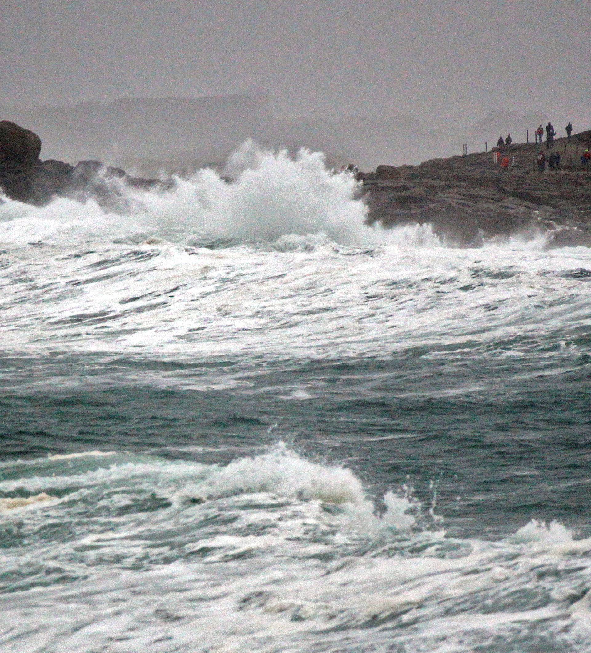 People standing on the Pointe de la Torch peninsula watch waves breaking on the Brittany coast after storm Eleanor hit Saint-Guenole