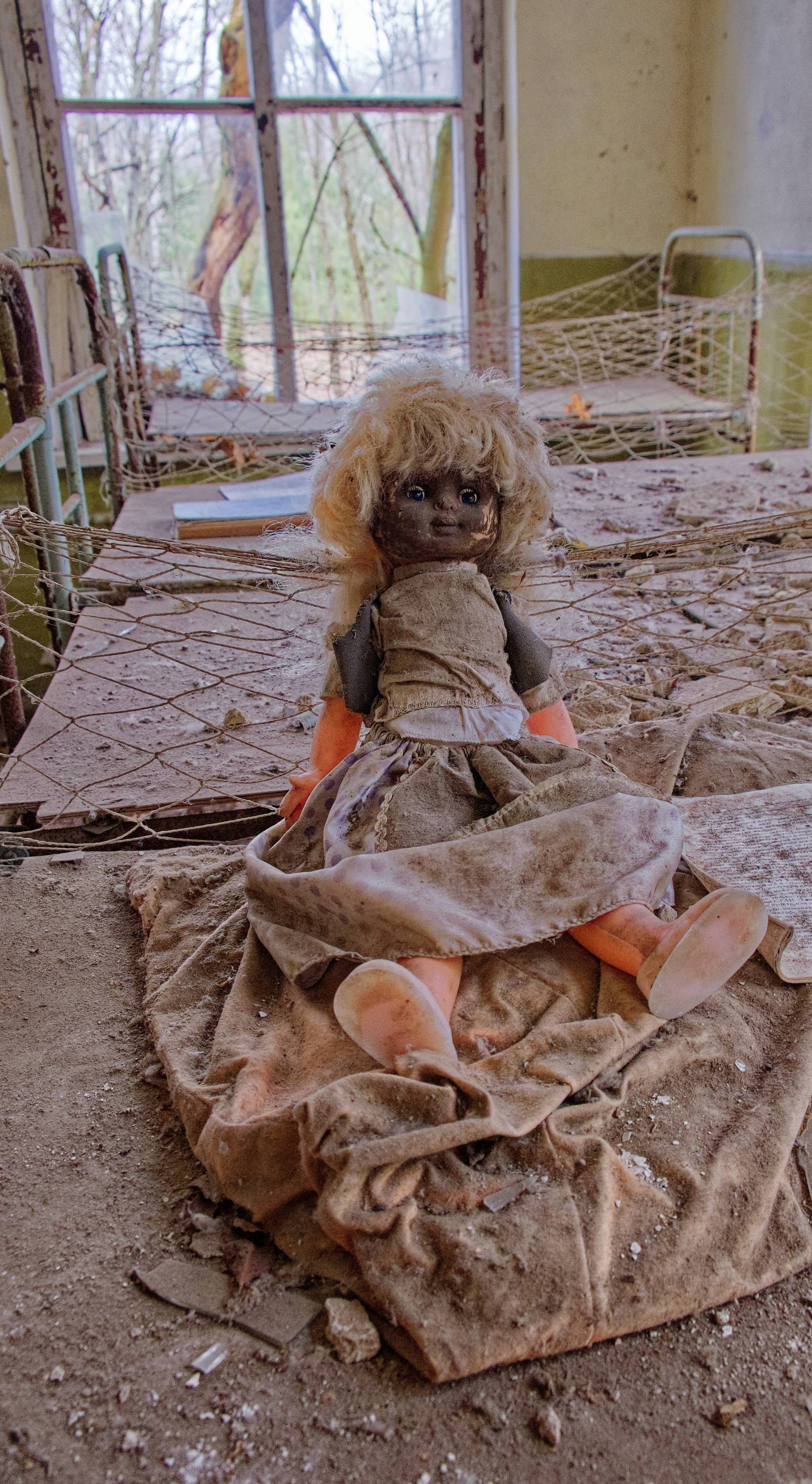 An abandoned room houses a doll with a sad expression. An old doll with a dirty face on a bed in an abandoned kindergarten. Radiation-contaminated room in Chernobyl.