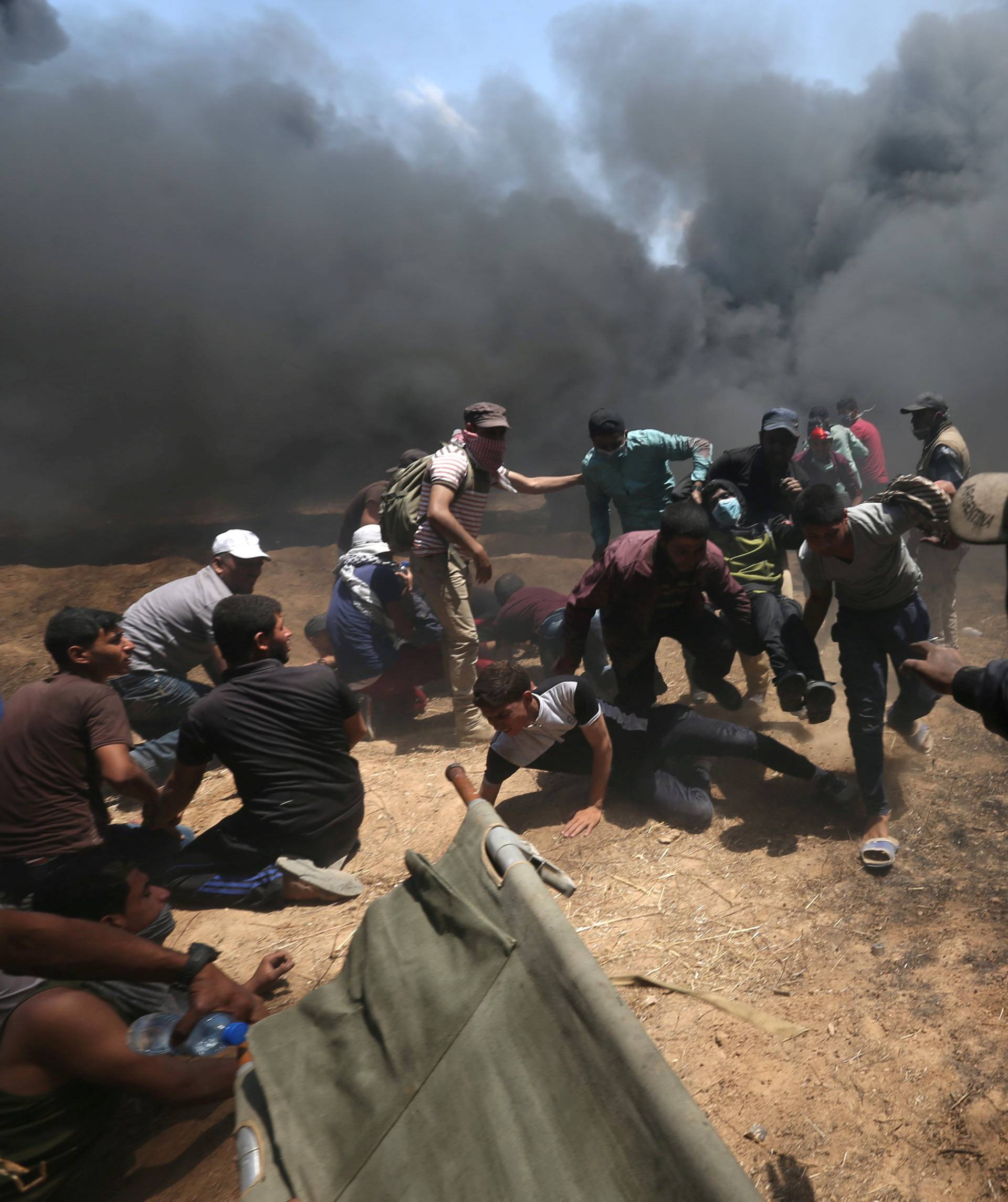 Wounded Palestinian demonstrator is evacuated as others take cover from Israeli fire and tear gas during a protest against U.S. embassy move to Jerusalem and ahead of the 70th anniversary of Nakba, at the Israel-Gaza border in the southern Gaza Strip